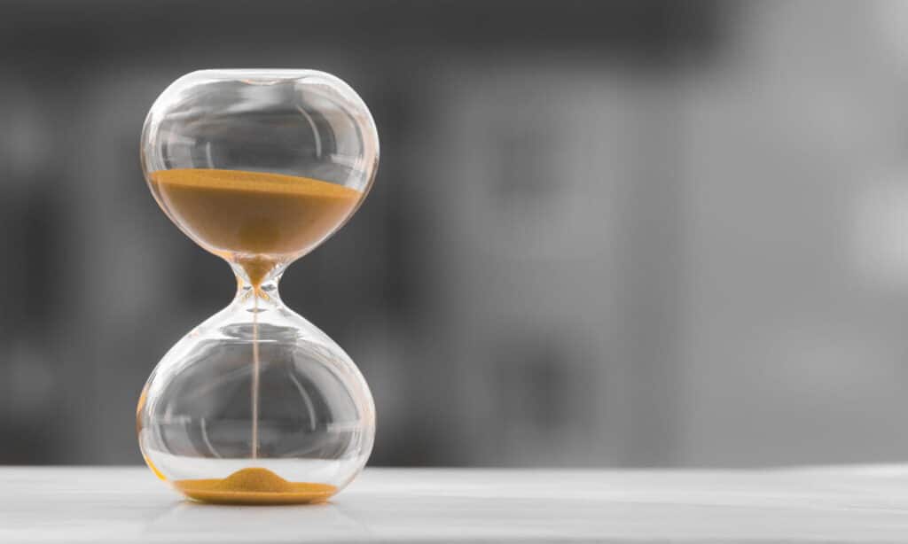 Hourglass with golden sand on a desk, representing timing the sale of a commercial property