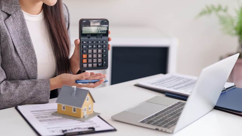 Property professional holding a calculator beside a model house and documents, representing commercial property valuation